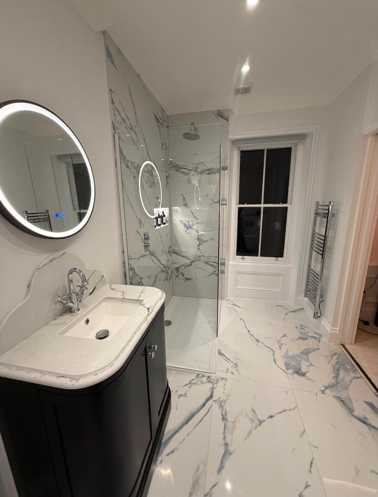 A finished bathroom by Carter of London — full marble-effect porcelain, walk-in shower, curved vanity unit and backlit mirror